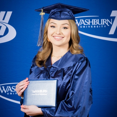 student in cap n gown smiling in front of Washburn Tech branded background